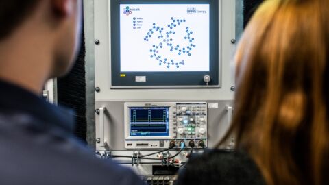 Man sieht zwei Menschen von hinten, die auf einen Bildschirm schauen.