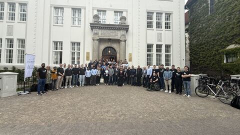 Eine Gruppe von Menschen steht auf dem Hof vor einem weißen Gebäude.