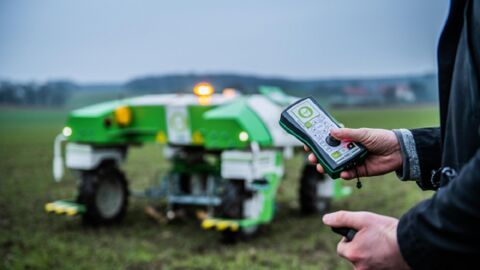 Person steuert landwirtschaftliches Fahrzeug mit einer Fernbedienung
