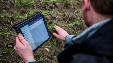 Mann hält Tablet in der Hand und berührt den Boden eines Ackers
