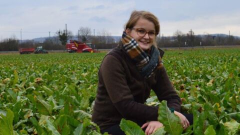 Frau hockt auf einem Feld und blickt in die Kamera