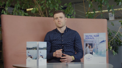 Ein Mann sitzt hinter einem Tisch, auf dem ZDIN Flyer stehen