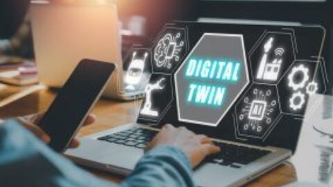 Person hält Handy und sitzt vor Laptop