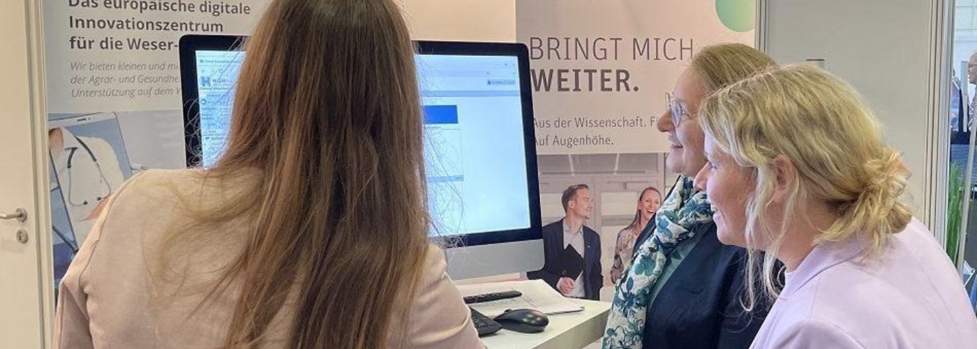 Drei Frauen stehen vor einem Bildschirm.